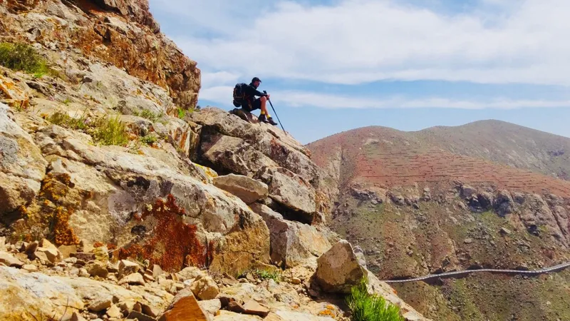 A walker resting on red volcanic rock high above a valley