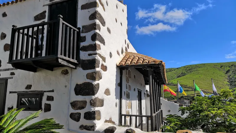 A white house with corners of dark volcanic stone and a wooden balcony