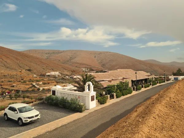The house beside the road into Betancuria, a car parked in front, bare brown mountains behind