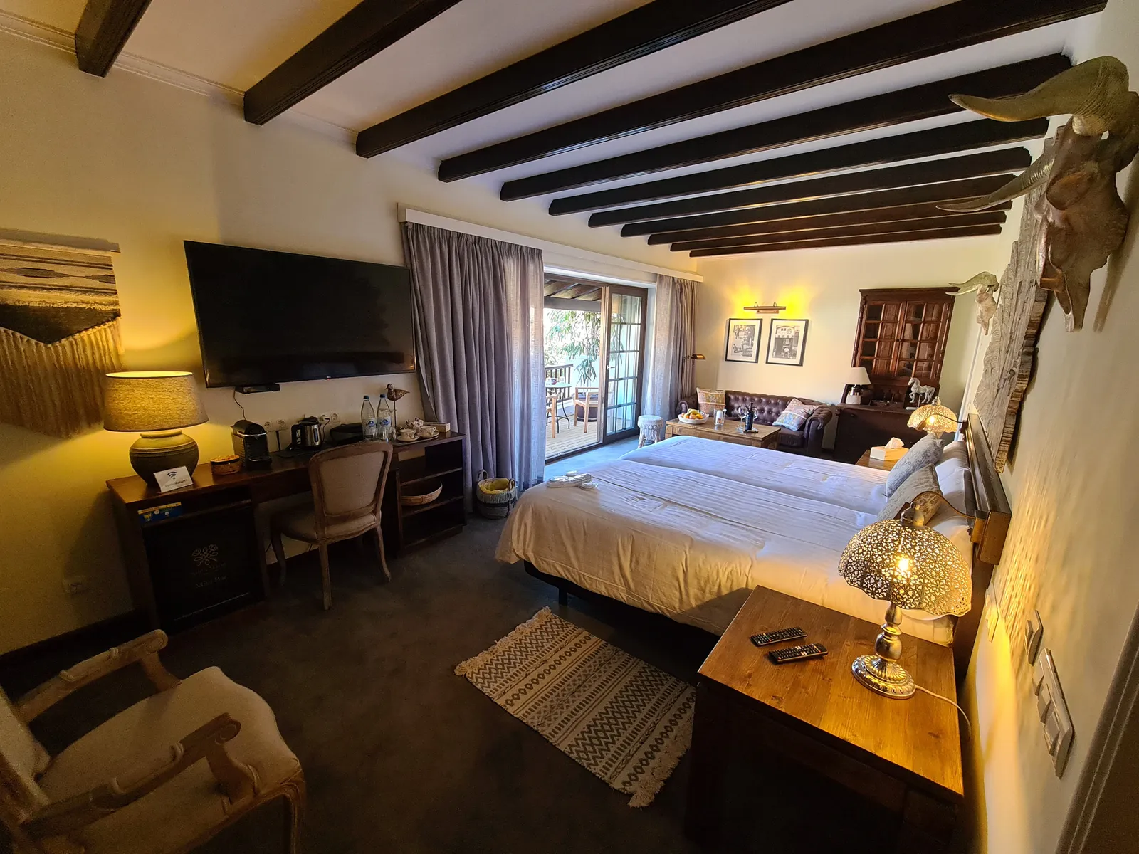 Junior Suite Nº 1: the bed under dark wooden beams, a desk and the sitting area by the terrace doors