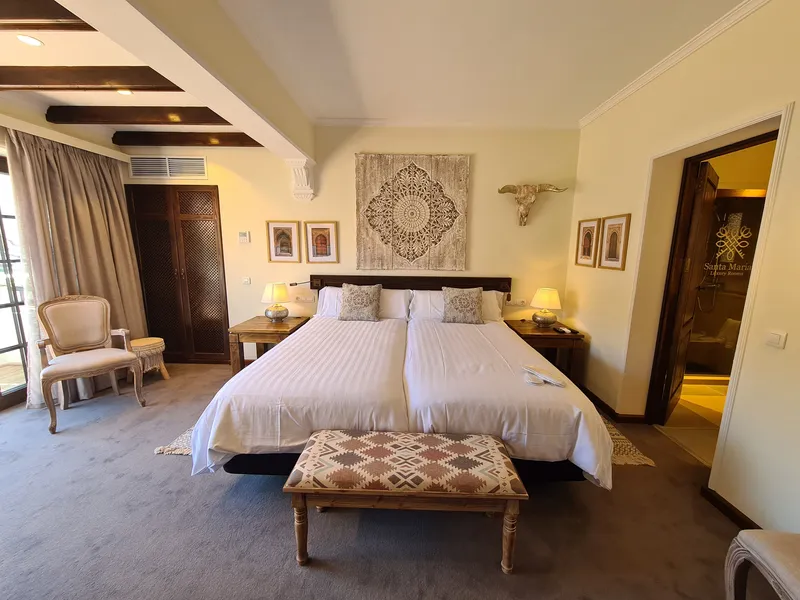 The beds beneath a carved ornament, with a patterned bench at their foot