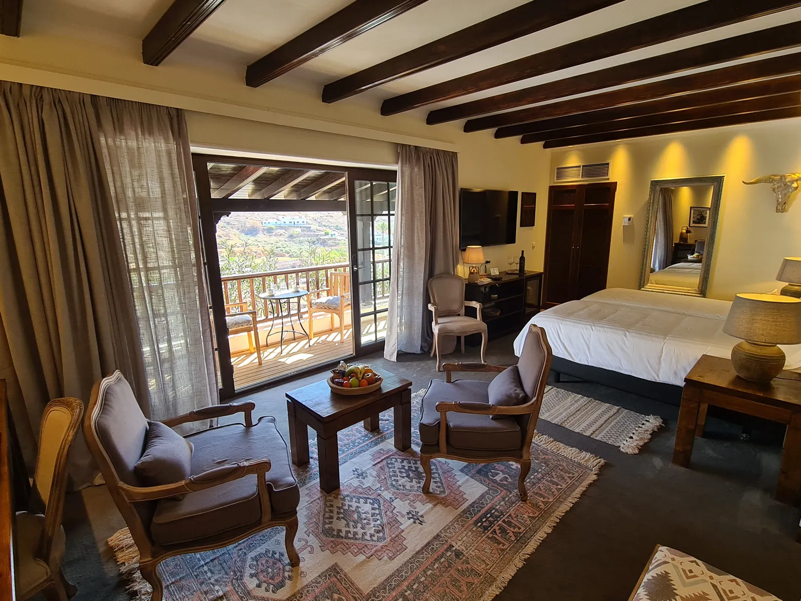 Junior Suite Nº 5: two armchairs on a woven rug, the bed and the doors to the covered balcony