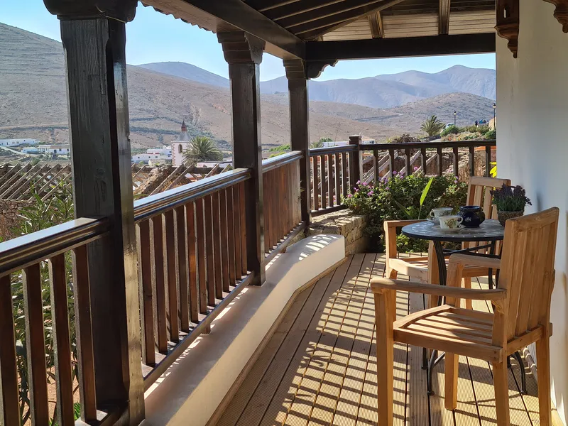 The long covered balcony of Junior Suite Nº 5 with wooden posts and chairs, the valley beyond