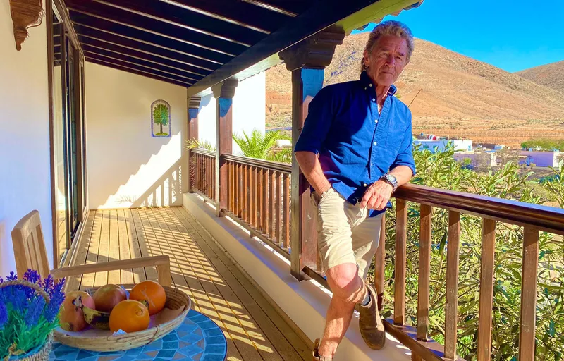 A man at the railing of the covered balcony, the hills behind