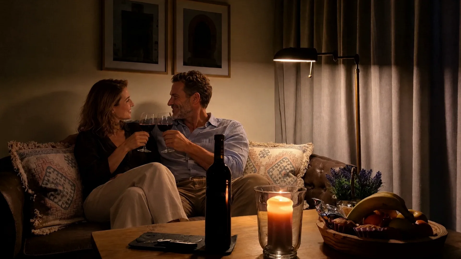 Evening in Double Room Nº 4: a couple raising glasses of red wine on the leather sofa, a bottle and a candle on the table